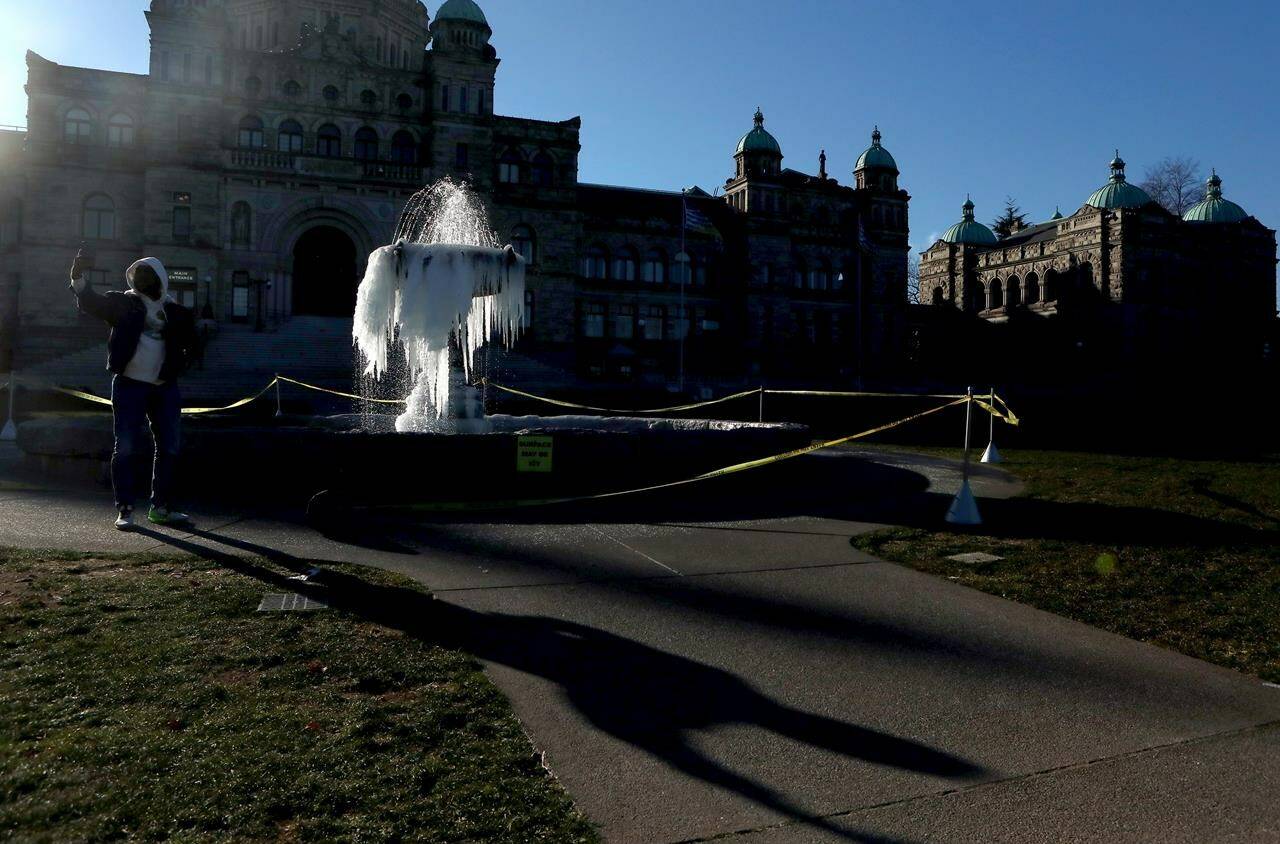 Cold temperatures across the province sets in as a man reflected off the Queen Victoria statue takes a picture of the fountain out front of the legislature freezes over during a cold spell in Victoria, B.C., on Friday, January 12, 2024. THE CANADIAN PRESS/Chad Hipolito