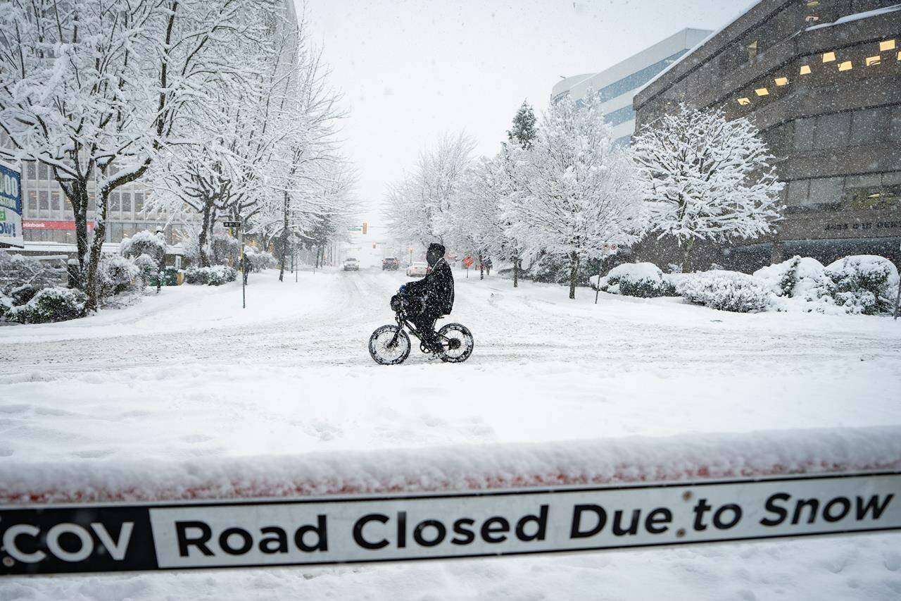A person cycles past a road closed sign during a snowstorm in Vancouver Wednesday, Jan. 17, 2024. A winter storm closed schools and disrupted flights in B.C. on Wednesday, with snow expected to continue in some parts of the province.THE CANADIAN PRESS/Ethan Cairns