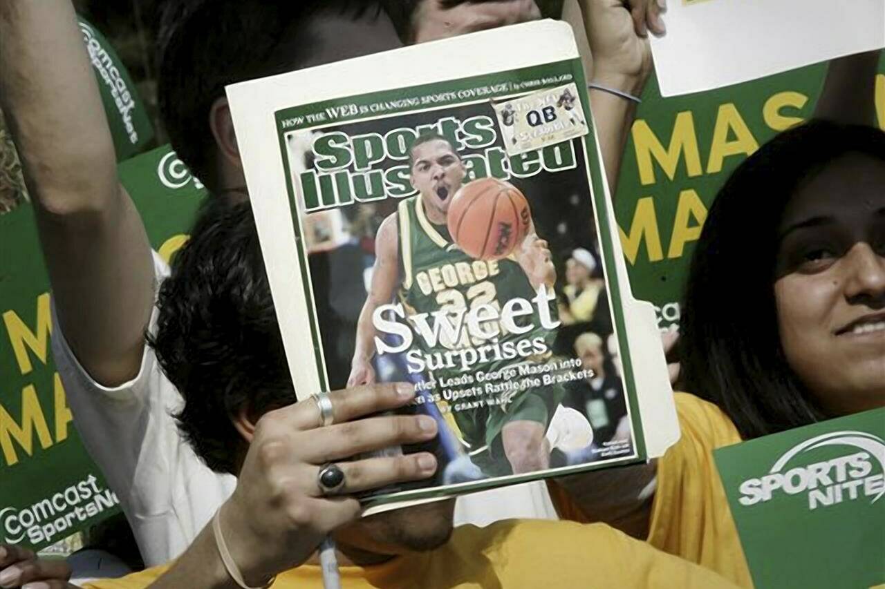 FILE - A George Mason University fan holds up the cover of Sports Illustrated magazine at a send off for the team, Wednesday, March 29, 2006, in Fairfax, Va. The publisher of Sports Illustrated has notified employees it is planning to lay off a significant portion — possibly all — of the outlet’s staff after its license to use the iconic brand’s name in print and digital was revoked. In an email to employees Friday morning, Jan. 19, 2024, the Arena Group, which operates Sports Illustrated and related properties, said that Authentic Brands Group has revoked its marketing license. (AP Photo/Lawrence Jackson, File)