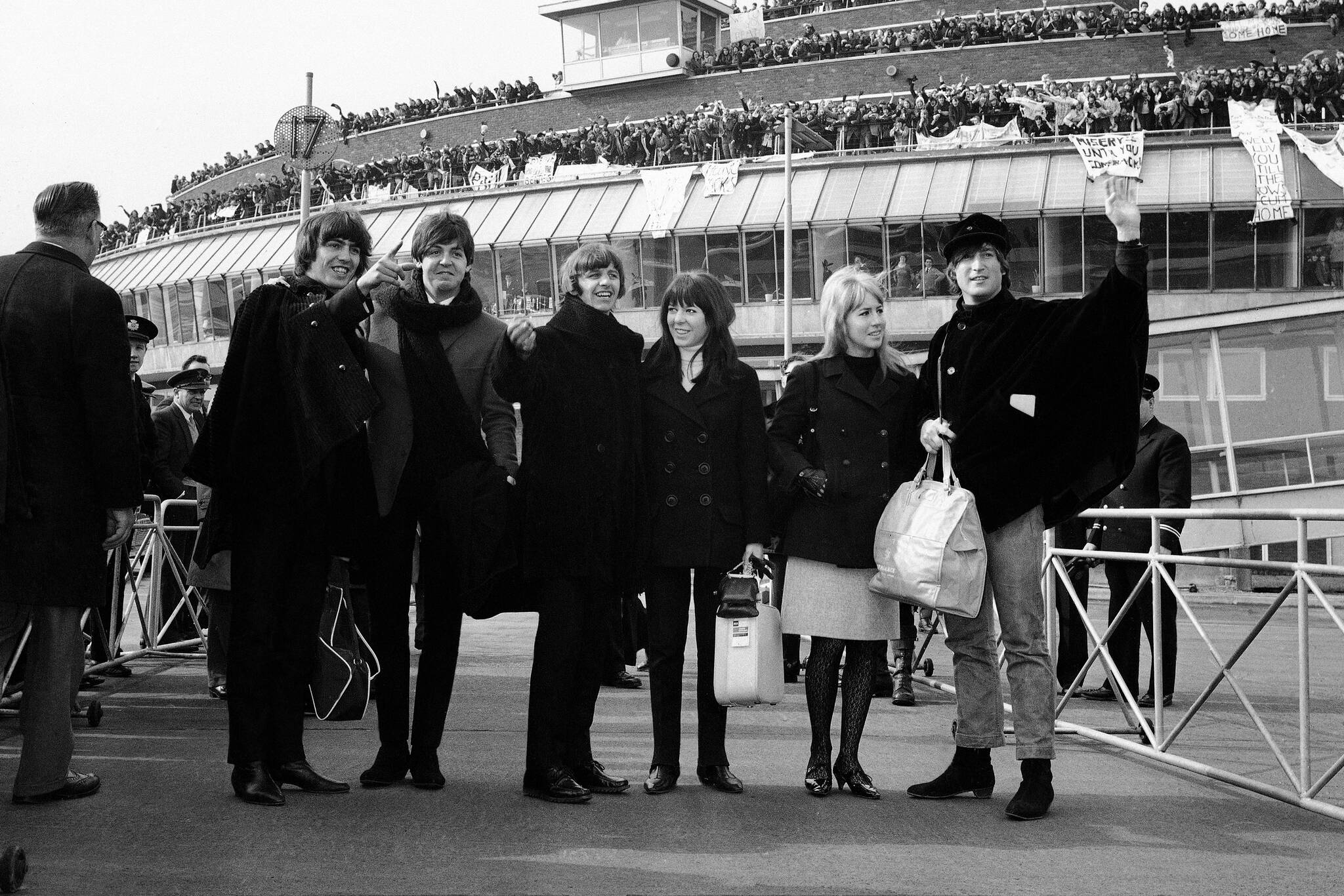 Fans covering the roof of a London Airport building cheer the Beatles as the group leave London, England on March 13, 1965, to fly to Salzburg, Austria, to continue work on their second film. From left are George Harrison; Paul McCartney; Ringo Starr; his wife, Maureen Starr; Cynthia Lennon, and husband John Lennon. (AP Photo/Victor Boynton)