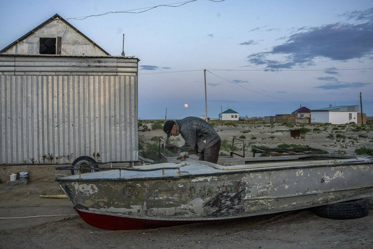 A man repairs an old boat along the dried-up Aral Sea, in the village of Tastubek near the Aralsk city, Kazakhstan, Monday, July 2, 2023. The demise of the once-mighty sea has affected thousands of residents and their livelihoods for decades. (AP Photo/Ebrahim Noroozi)