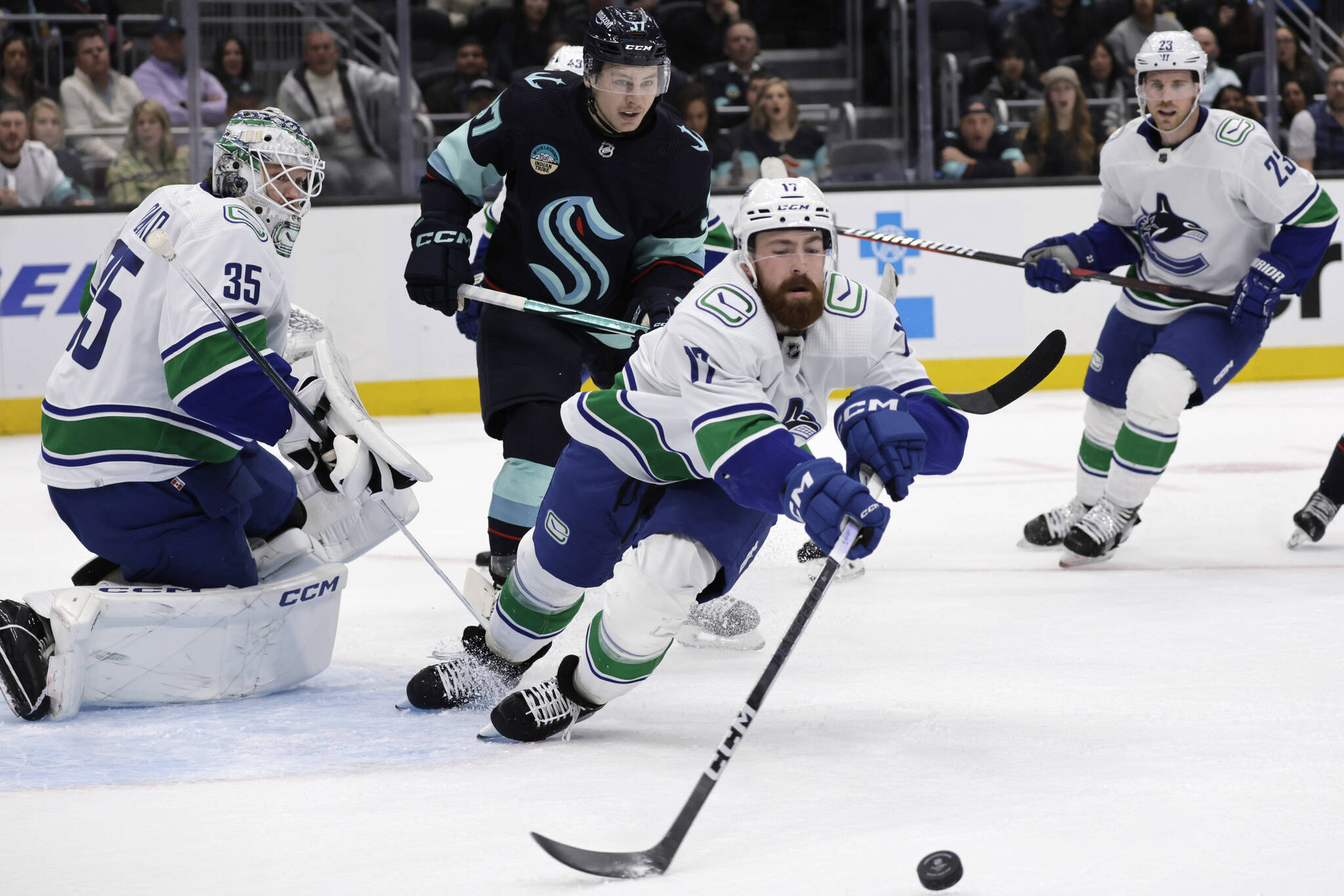Vancouver Canucks defenseman Filip Hronek reaches for a blocked shot by goaltender Thatcher Demko with Seattle Kraken center Yanni Gourde skating behind during the first period of an NHL hockey game, Thursday, Feb. 22, 2024, in Seattle. (AP Photo/John Froschauer)