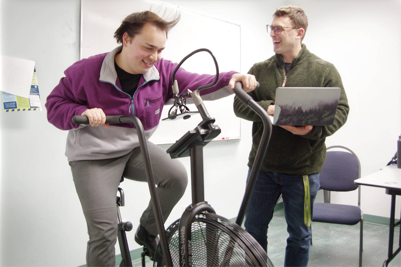 Research assistant Andrew Szilogyi whips up some wind on a stationary air-resistance bike while psychology student Derek LeBaron enters notes on his laptop computer at Vancouver Island University. LeBaron is researching how various forms of social support impact exercise performance. (Chris Bush/News Bulletin)