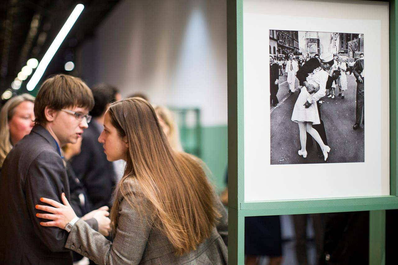 FILE - People speak next to a famous photograph taken by Alfred Eisenstaedt of a sailor kissing a nurse in New York’s Times Square on V-J Day at the Jewish Museum and Tolerance Center in Moscow on April 14, 2015. Veterans Affairs Secretary Denis McDonough has reversed a department memo shared by a VA undersecretary Tuesday, March 5, 2024, that aimed to ban VA displays of the iconic photograph because it “depicts a non-consensual act” and was inconsistent with the department’s sexual harassment policy. (AP Photo/Alexander Zemlianichenko, File)