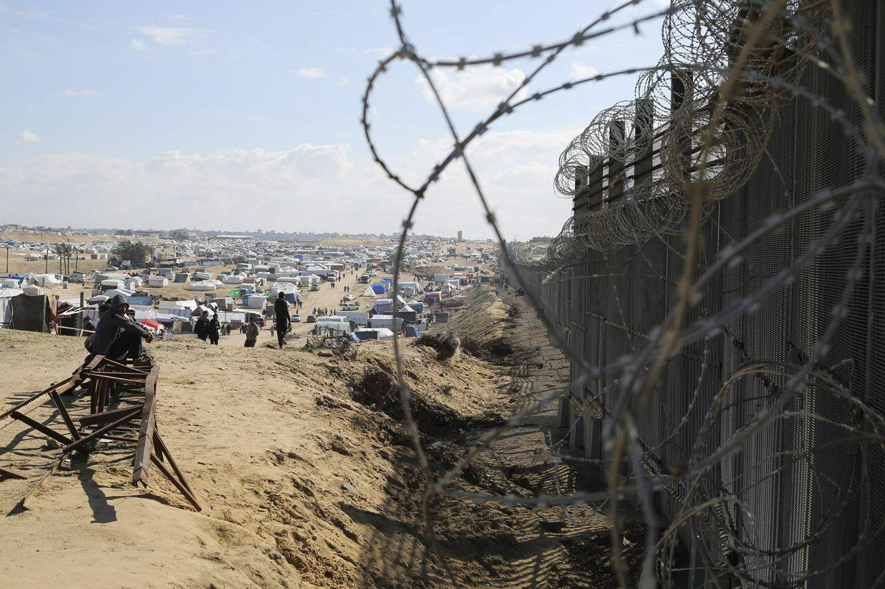 Palestinians displaced by the Israel air and ground offensive on the Gaza Strip sit next to the border fence with Egypt in Rafah, Wednesday, Jan. 24, 2024. THE CANADIAN PRESS/AP-Hatem Ali