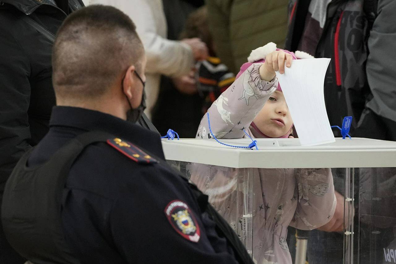 A child casts his parent’s ballot as a police officer guards at a polling station during the presidential election in St. Petersburg, Russia, Sunday, March 17, 2024. Voters in Russia are going to the polls for the last day of a presidential election that is all but certain to extend President Vladimir Putin’s rule after he clamped down on dissent. (AP Photo/Dmitri Lovetsky)