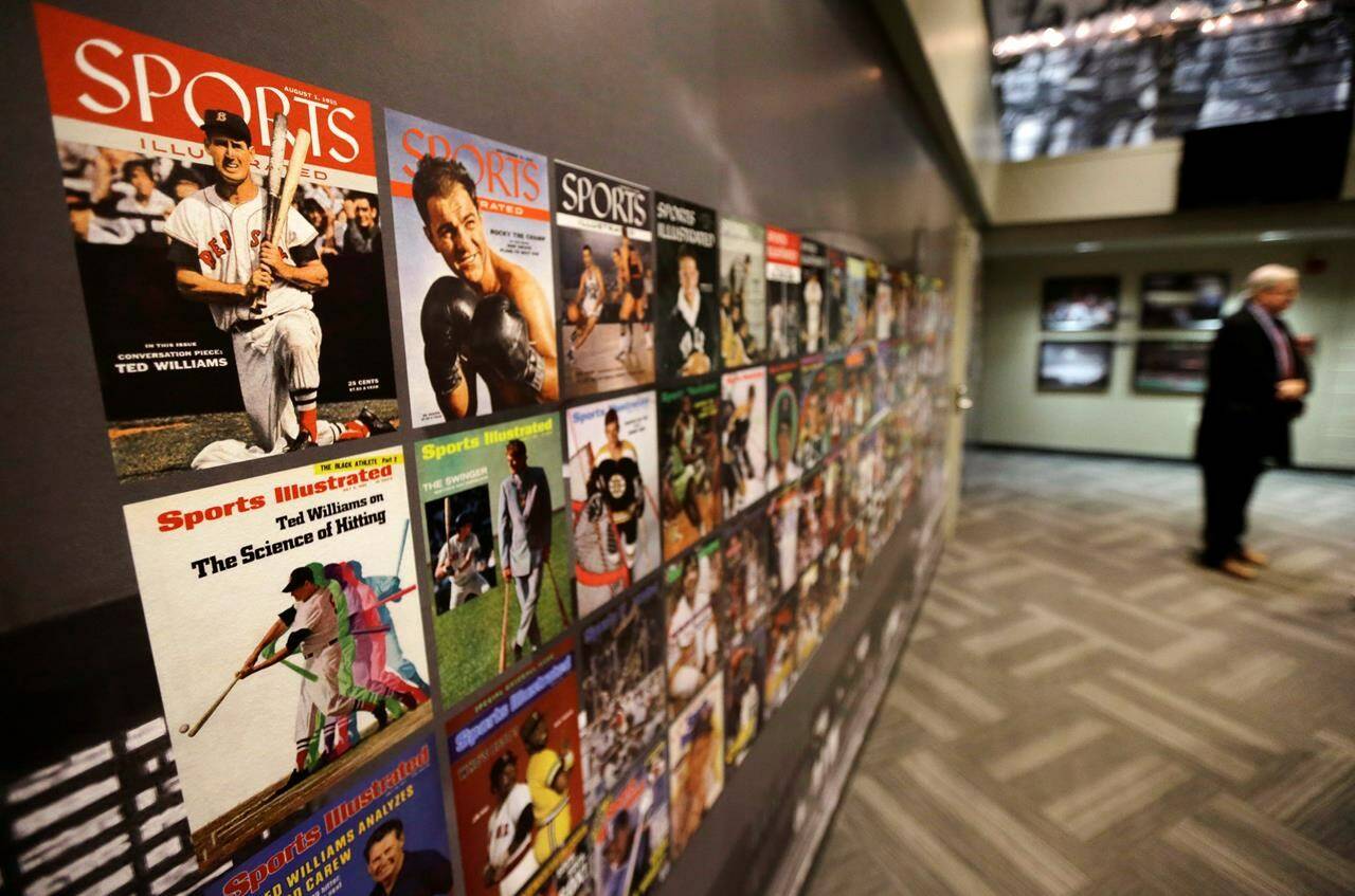FILE - The Sports Museum curator Richard Johnson, right, stands near an exhibit that displays cover photos from the sports magazine Sports Illustrated in the museum at the TD Garden, in Boston, Dec. 17, 2015. Sports Illustrated will continue operations after the company that owns the brand reached an agreement with a new publisher for its print and digital products, Monday, March 18, 2024. (AP Photo/Steven Senne, File)