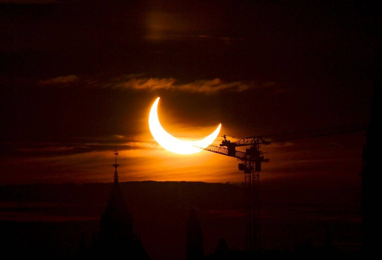 An annular solar eclipse rises over construction cranes and the Peace Tower on Parliament Hill in Ottawa on Thursday, June 10, 2021. A total solar eclipse is a rare celestial event that always generates excitement, but next month’s version is expected to be unusually spectacular. THE CANADIAN PRESS/Sean Kilpatrick