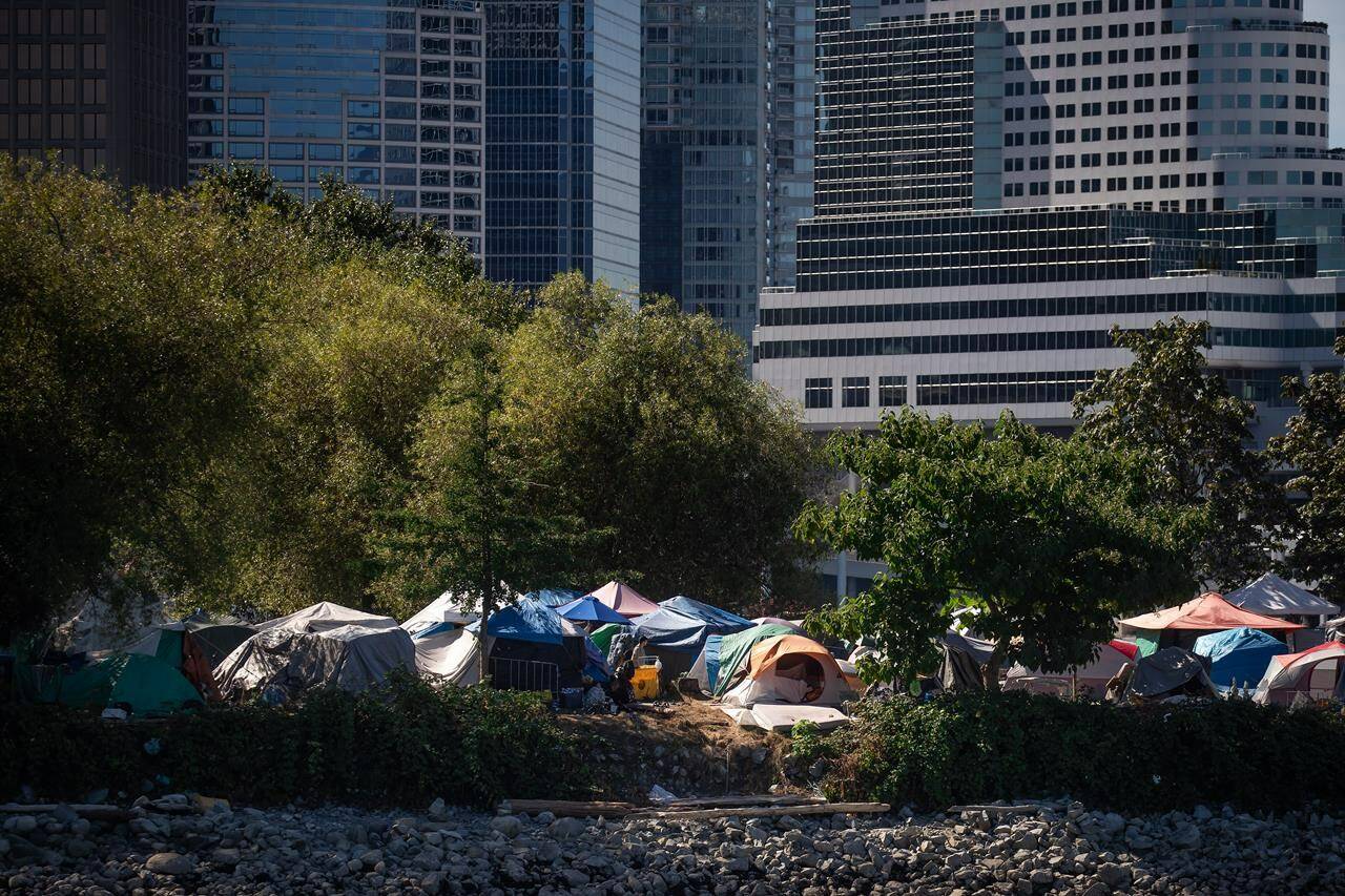 Tents and people are seen at a homeless encampment at Crab Park below the towers of the downtown skyline in Vancouver on Aug. 14, 2022. THE CANADIAN PRESS/Darryl Dyck