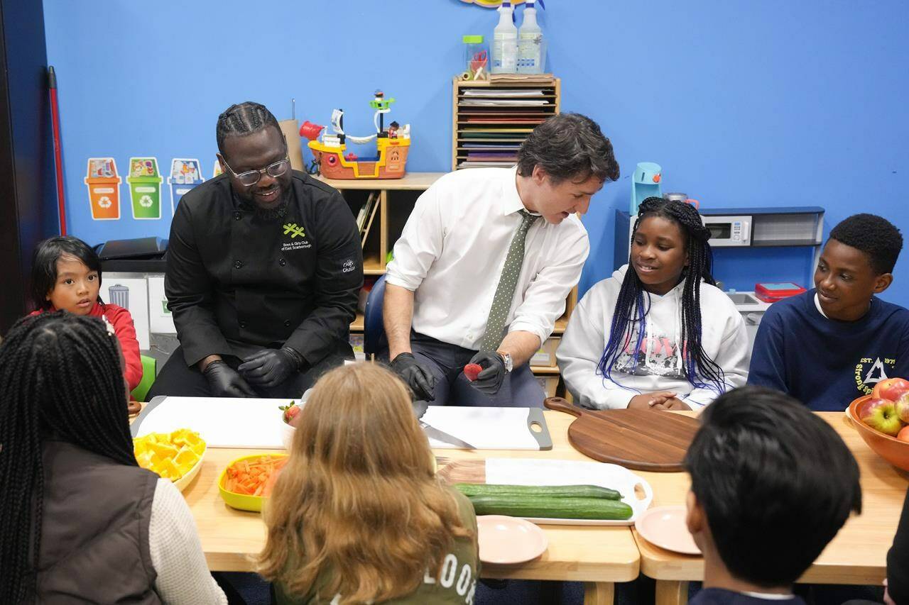 Prime Minister Justin Trudeau talks to ten year old Chakai as he cuts fruit next to chef Jason Simpson while preparing food for a lunch program at the Boys and Girls Club East Scarborough, in Toronto, Monday, April 1, 2024. Trudeau says the upcoming federal budget will include funding for a national school food program that aims to provide meals to 400,000 more kids per year across the country. THE CANADIAN PRESS/Chris Young