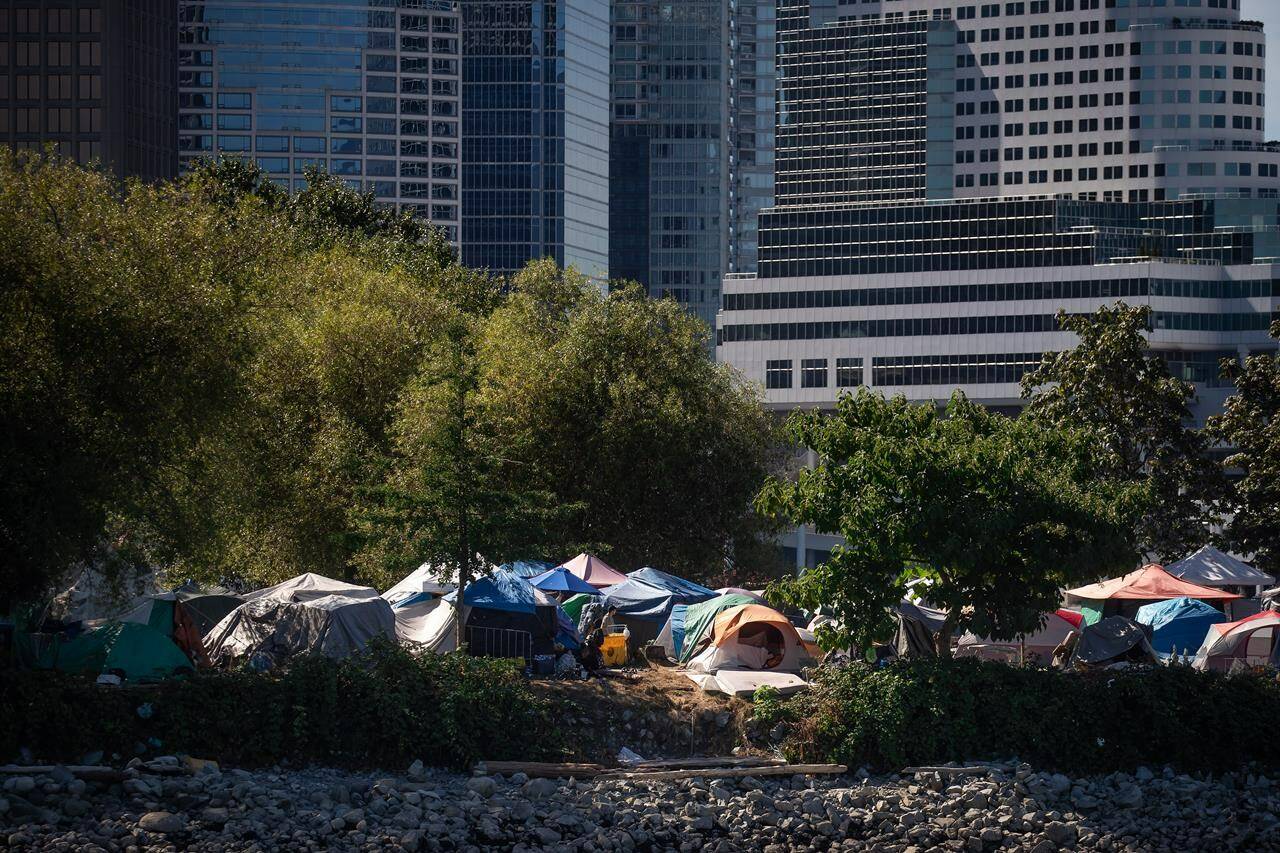 Tents and people are seen at a homeless encampment at Crab Park below the towers of the downtown skyline in Vancouver on Sunday, August 14, 2022. Residents forced out of a Vancouver homeless encampment will be allowed back in this week after the city completed a cleanup of the site. THE CANADIAN PRESS/Darryl Dyck