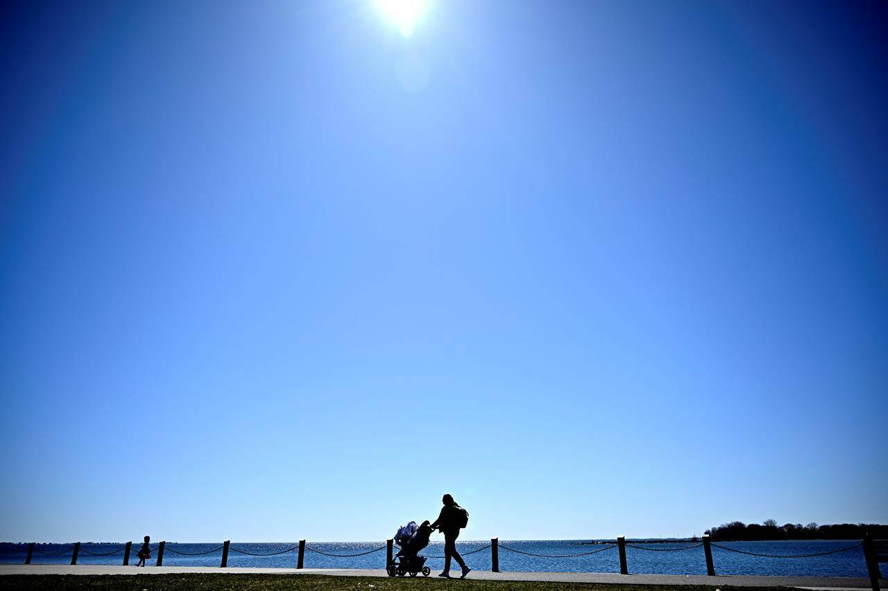 A total solar eclipse is set to fall over parts of Canada, gathering massive crowds in its path who hope to catch a glimpse of the rare celestial event. A blue sky shines below the sun as a person walks with an infant along the shores of Lake Ontario, a day before a total solar eclipse will be visible in Kingston, Ont., Sunday, April 7, 2024. THE CANADIAN PRESS/Justin Tang