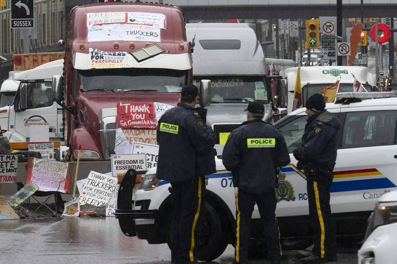 A parliamentary committee reviewing Ottawa’s use of the Emergencies Act has set a date to get back to drafting a report that was initially due in December 2022. Police officers keep an eye on protest trucks, in Ottawa, Thursday, Feb. 17, 2022. THE CANADIAN PRESS/Adrian Wyld