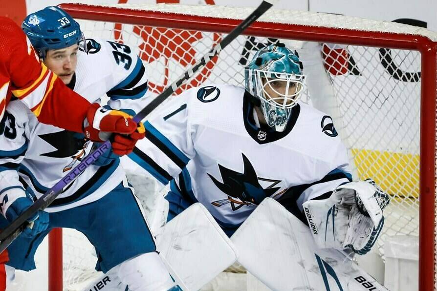San Jose Sharks defenceman Calen Addison (33) checks Calgary Flames forward Martin Pospisil (76) as goalie Devin Cooley (1) follows the play during second period NHL hockey action in Calgary, Thursday, April 18, 2024. THE CANADIAN PRESS/Jeff McIntosh
