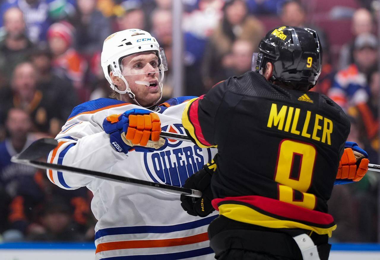 Edmonton Oilers' Connor McDavid, back left, checks Vancouver Canucks' J.T. Miller during the third period of an NHL hockey game in Vancouver, on Monday, November 6, 2023. THE CANADIAN PRESS/Darryl Dyck