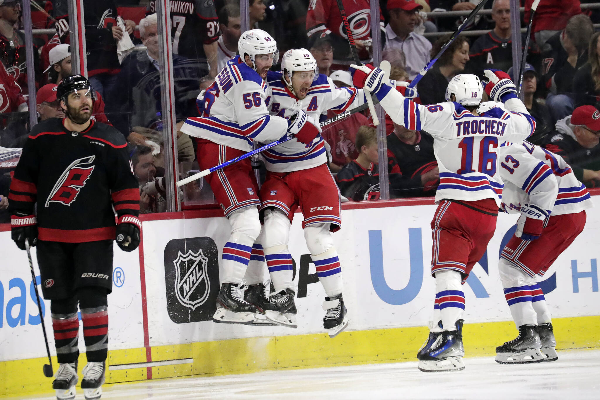 New York Rangers defenseman Erik Gustafsson (56), left wing Artemi Panarin, center Vincent Trocheck (16) and left wing Alexis Lafrenière (13) celebrate after scoring the winning goal in the overtime period in Game 3 of an NHL hockey Stanley Cup second-round playoff series Thursday, May 9, 2024, in Raleigh, N.C. Carolina Hurricanes left wing Jordan Martinook skates away at left. (AP Photo/Chris Seward)