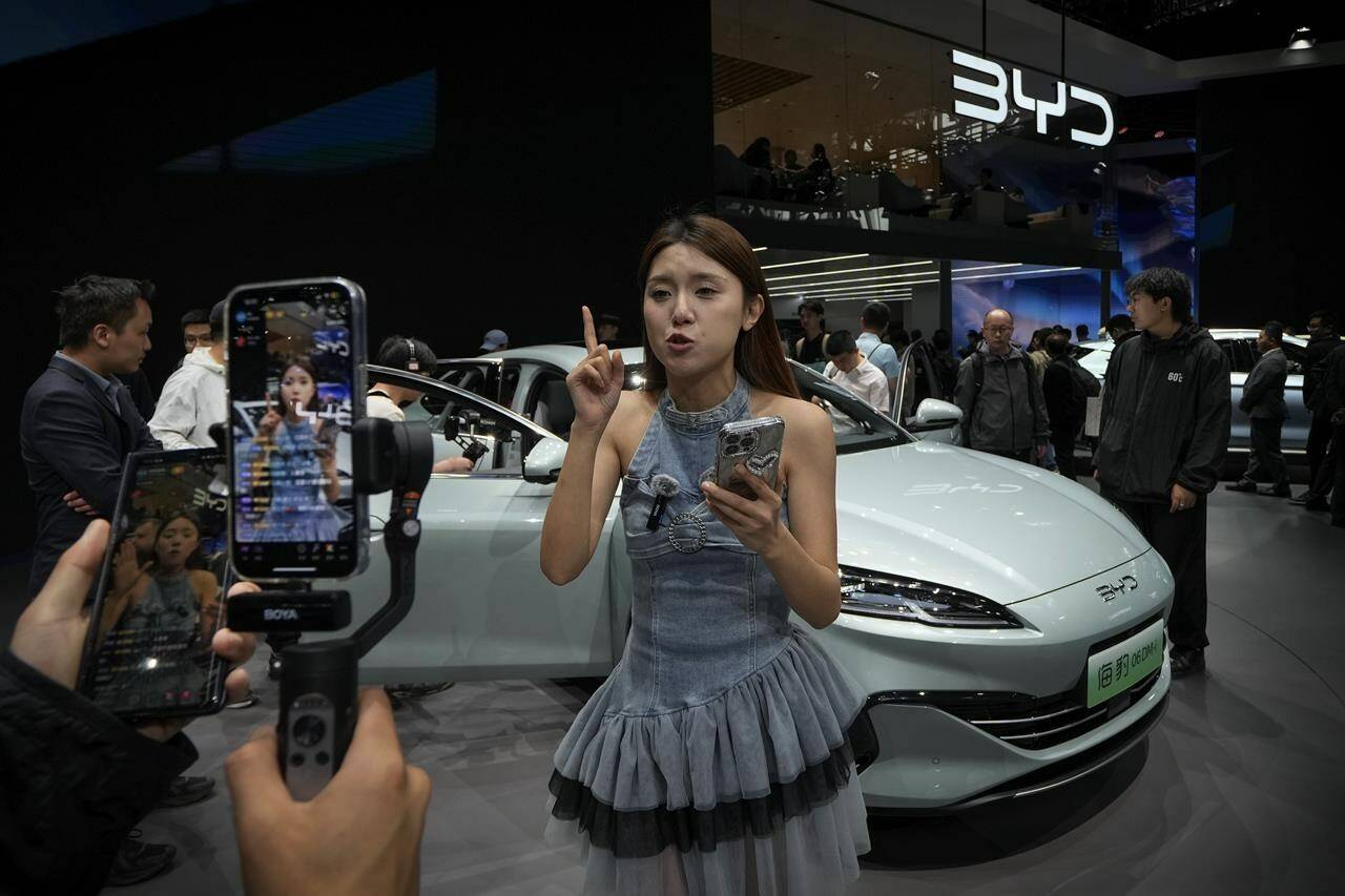 A model performs a live-streaming near a BYD Sea Leopard DM-i car model during the Auto China 2024 in Beijing, Sunday, April 28, 2024. Global automakers and EV startups unveiled new models and concept cars at China’s largest auto show, with a focus on the nation’s transformation into a major market and production base for digitally connected, new-energy vehicles. (AP Photo/Andy Wong)