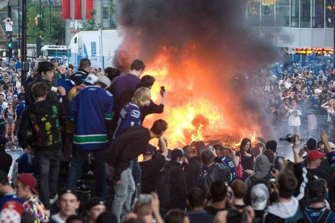 Vancouver Canucks fans watch a car burn during a riot following game 7 of the NHL Stanley Cup final in downtown Vancouver, on June 15, 2011. THE CANADIAN PRESS/Geoff Howe