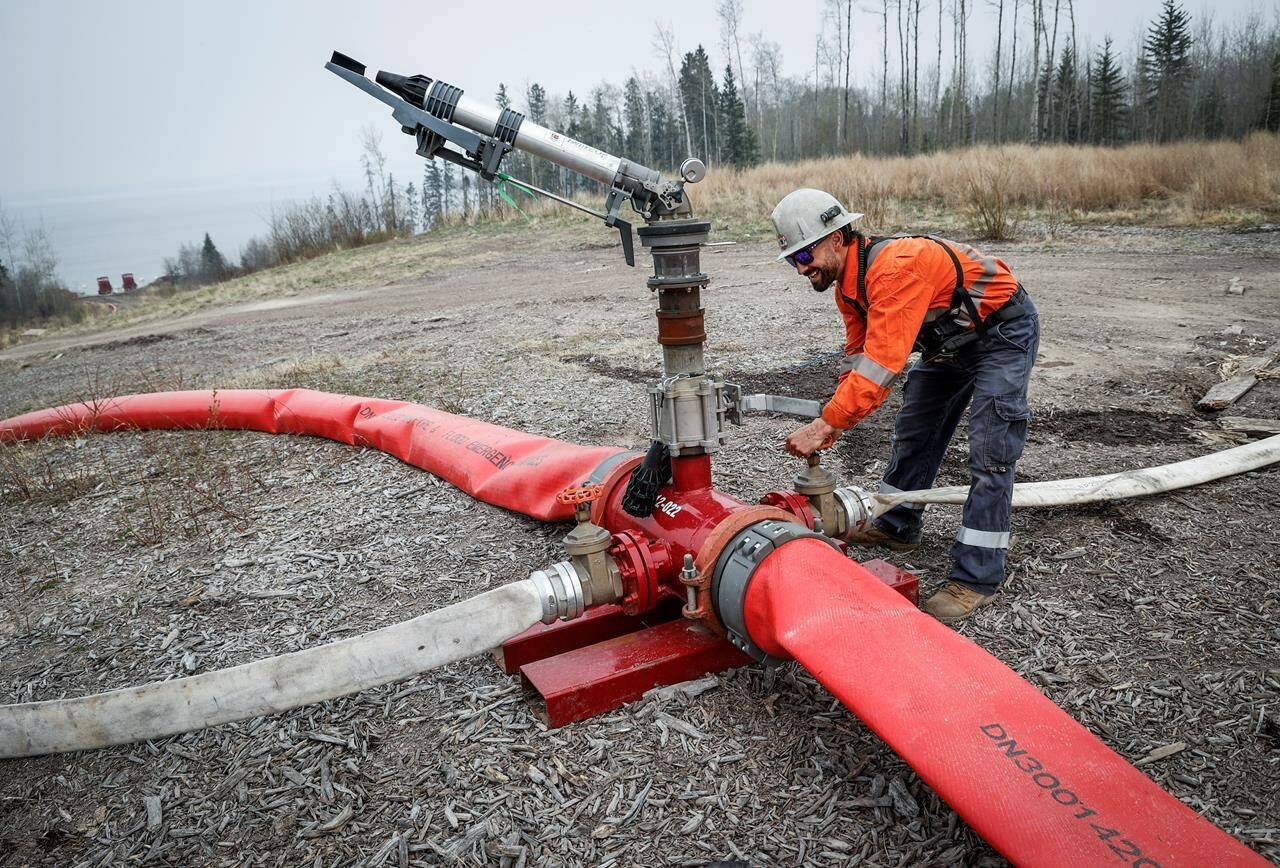Justin Massie, wildfire specialist with Fire & Flood Emergency Service Ltd., adjusts a valve on a wildfire suppression water cannon along Highway 881 near Gregoire Lake Estates southeast of Fort McMurray, Wednesday, May 15, 2024.THE CANADIAN PRESS/Jeff McIntosh