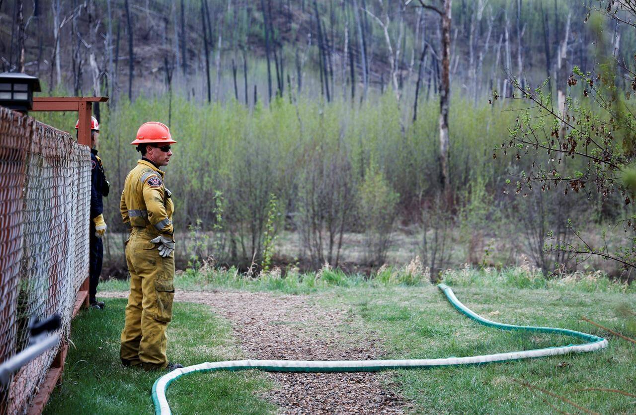 A firefighters monitors a wildfire sprinkler hose in the evacuated neighbourhood of Grayling Terrace in Fort McMurray, Alta., Thursday, May 16, 2024. THE CANADIAN PRESS/Jeff McIntosh