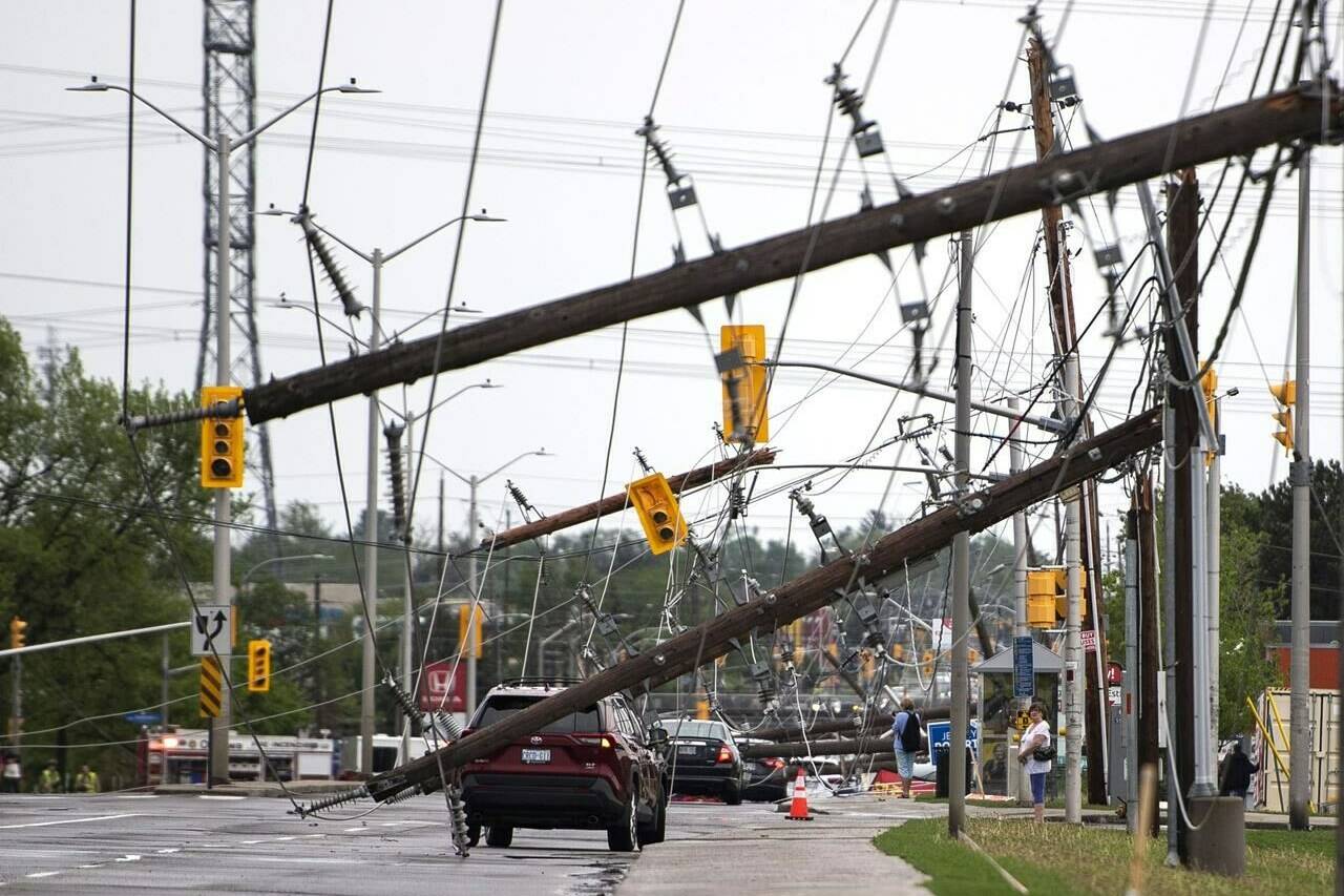 A vehicle is seen among downed power lines and utility poles after a major storm on Merivale Road in Ottawa on Saturday, May 21, 2022. The Local Leadership for Climate Adaptation initiative will offer up to $1 million to local governments for projects that upgrade or adjust their infrastructure and natural environment to be more protected from extreme weather events including floods, fires and major storms. THE CANADIAN PRESS/Justin Tang