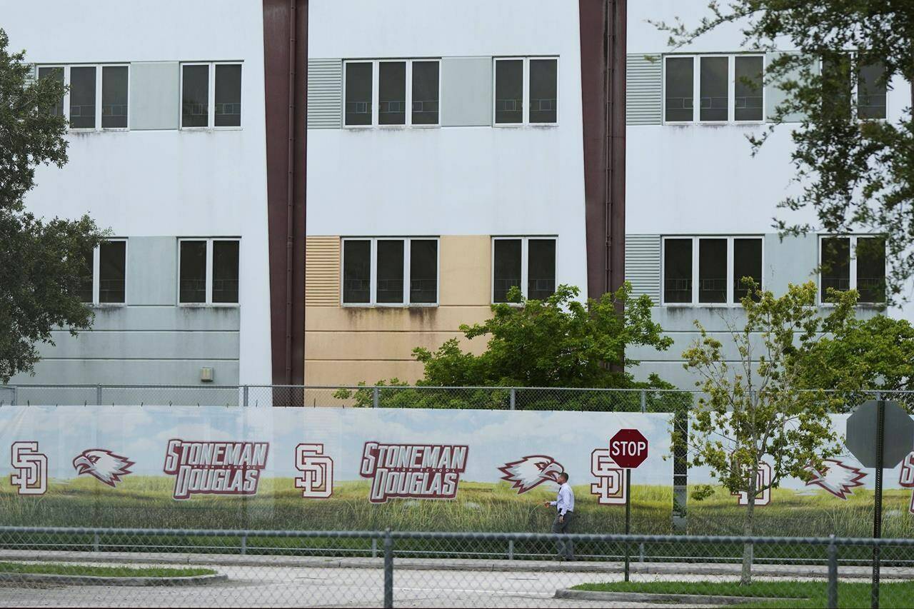 A security agent walks alongside a barrier surrounding Marjory Stoneman Douglas High School, July 5, 2023, in Parkland, Fla. Demolition of the building where 17 people died in the 2018 Parkland school shooting is set to begin, as crews will begin tearing down the three-story building at the high school on Thursday, June 13, 2024. (AP Photo/Rebecca Blackwell, File)