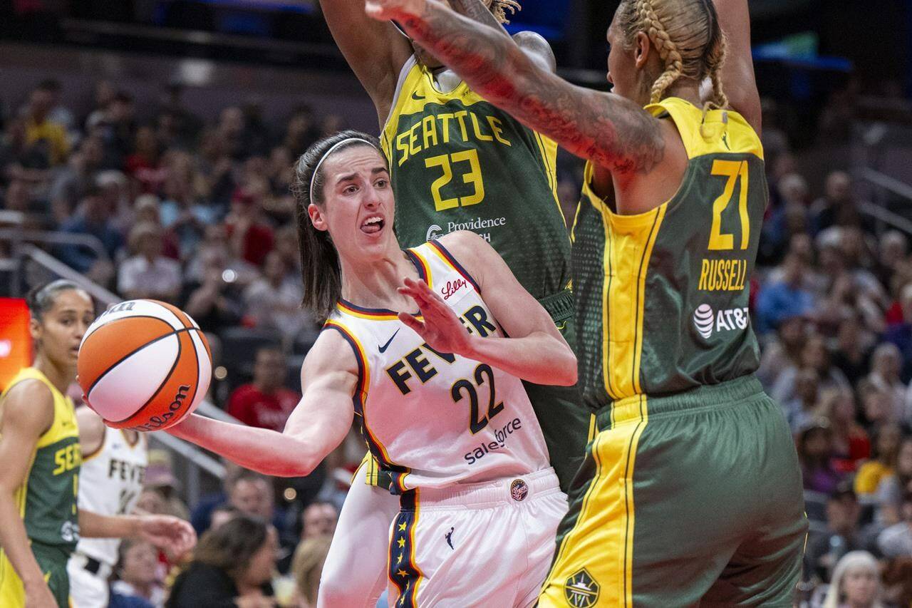 FILE - Indiana Fever guard Caitlin Clark (22) passes the ball from under the basket while being defended by Seattle Storm guard Jordan Horston (23) and center Mercedes Russell (21) during the first half of a WNBA basketball game, May 30, 2024, in Indianapolis. Not even a WNBA basketball game is an escape from the arguments and polarization that are so common in American life these days. (AP Photo/Doug McSchooler, File)