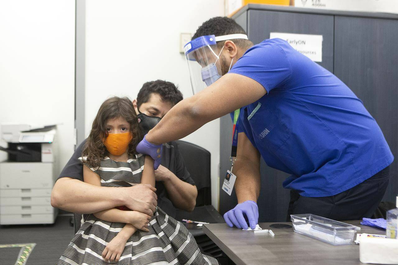 Seven-year-old Mabel Limdao is held by her father William as Dr. Kevin Evelyn of UHN gives her a COVID-19 vaccine at a “Kids and Families Vaccine Clinic” operated by Black Creek Community Health Centre and hosted by Jane and Finch EarlyON child and Family Centre in the Jane and Finch Mall in Toronto on Thursday, January 13, 2022. THE CANADIAN PRESS/Chris Young