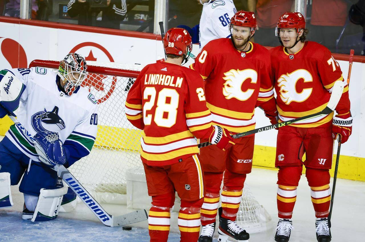 Vancouver Canucks goalie Collin Delia, left, clears the puck from the net as Calgary Flames forward Jonathan Huberdeau, centre right, celebrates his goal with teammates forward Elias Lindholm and forward Tyler Toffoli, right, during second period NHL pre-season hockey action in Calgary, Alta., Sunday, Sept. 25, 2022. THE CANADIAN PRESS/Jeff McIntosh