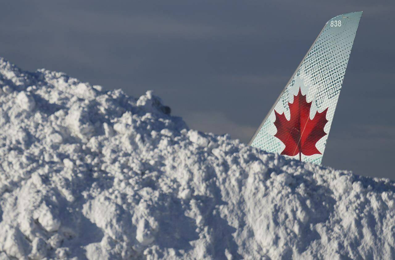 The tail of an Air Canada aircraft is seen behind a pile of snow at Vancouver International Airport in Richmond, B.C., Wed., Dec. 21, 2022. Environment Canada says the snow is not yet done with parts of the south coast. THE CANADIAN PRESS/Darryl Dyck
