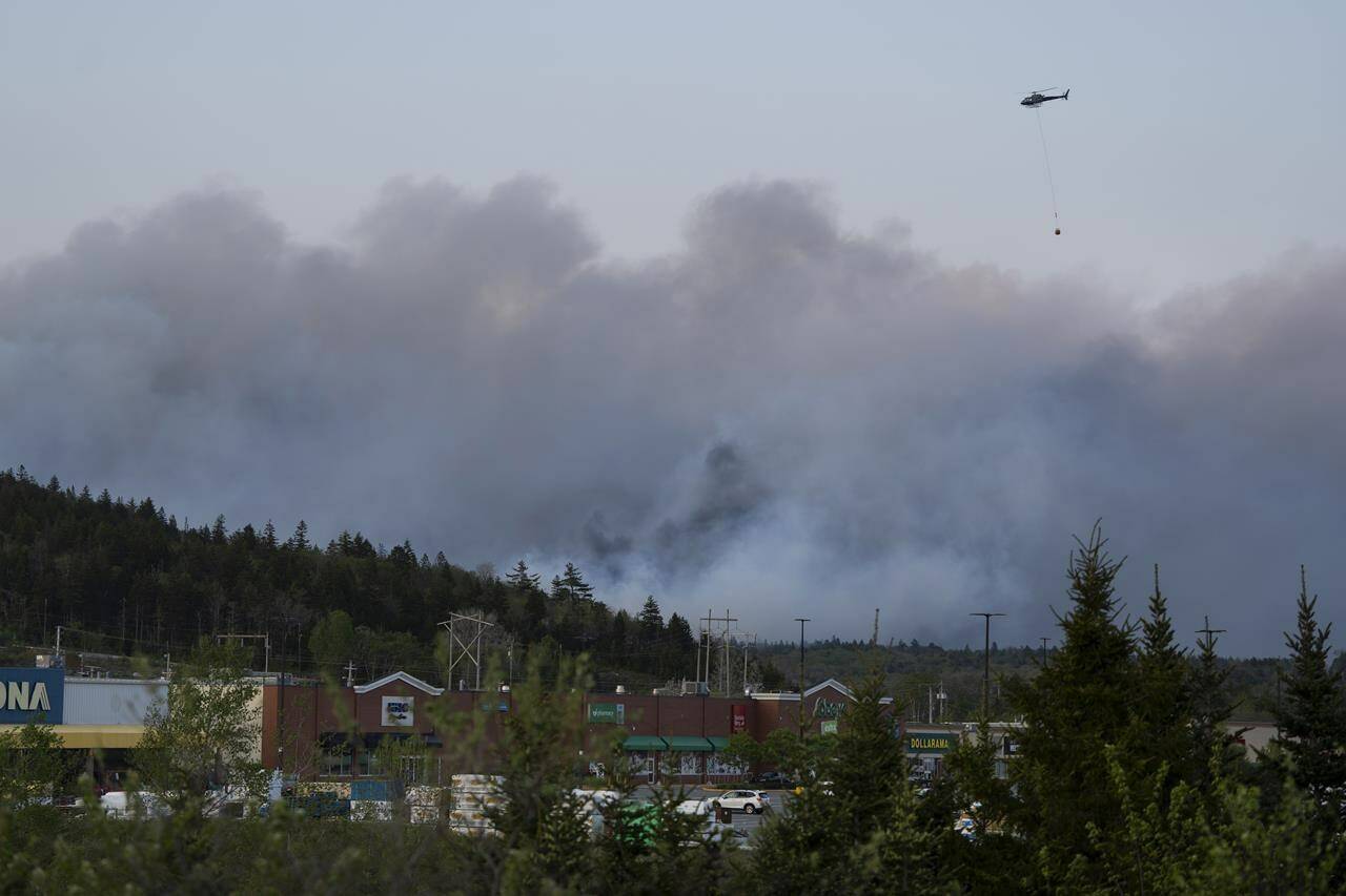 A helicopter carrying water flies over heavy smoke from an out-of-control fire in a suburban community outside of Halifax that spread quickly, engulfing multiple homes and forcing the evacuation of local residents on Sunday May 28, 2023.THE CANADIAN PRESS/Darren Calabrese