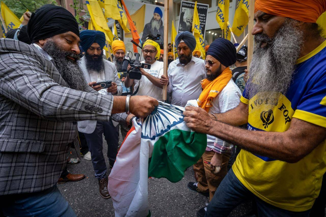 Two protestors try to rip the Indian flag after setting it on fire outside of the Consulate General of India Office during a protest for the recent shooting of Hardeep Singh Nijjar in Vancouver on Saturday, June 24, 2023. THE CANADIAN PRESS/Ethan Cairns