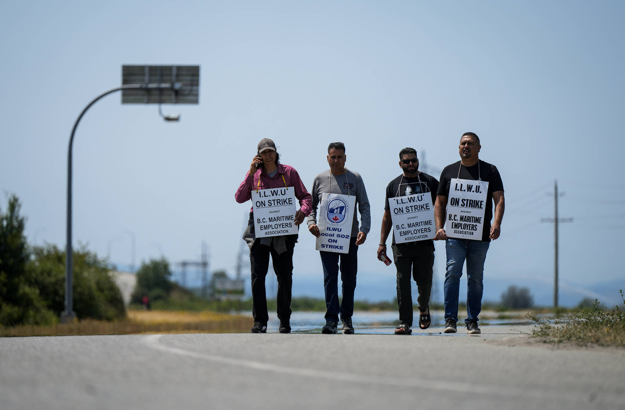 Striking International Longshore and Warehouse Union Canada workers walk a picket line on a road leading to Deltaport, in Delta, B.C., on Friday, July 7, 2023. THE CANADIAN PRESS/Darryl Dyck